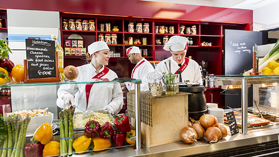 Two sodexo chefs pouring liquid in to a saucepan