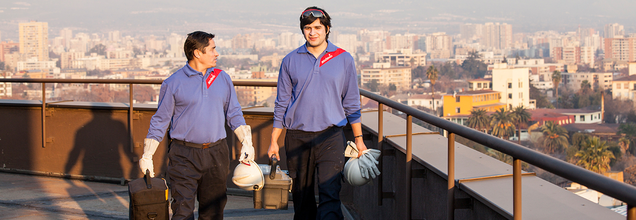 Two Sodexo employees standing on a roof in overalls, googles and hard hats